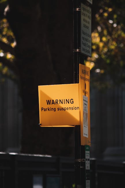A green and white parking restriction sign mounted on a metal pole with visible rust spots, indicating a two-hour parking limit from 8 am to 8 pm, Monday to Saturday, excluding Sundays. The sign is outdoors under a partly cloudy sky, with blurred green trees in the background. The sign's purpose is to inform drivers of parking rules, which is relevant for house removals and moving services like those offered by Man with Van Haringey, as they plan logistics for home relocation or furniture transport within local regulations.